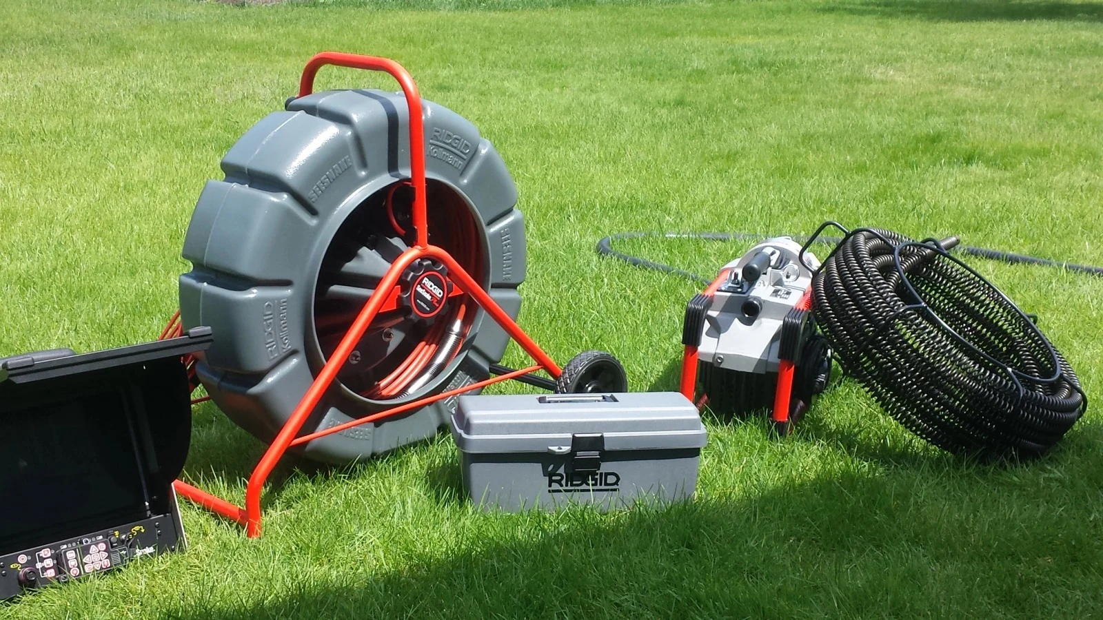 A Groess Underground equipment laid out on grass: a RIDGID SeeSnake camera reel and monitor, a drain machine and a coil of cable